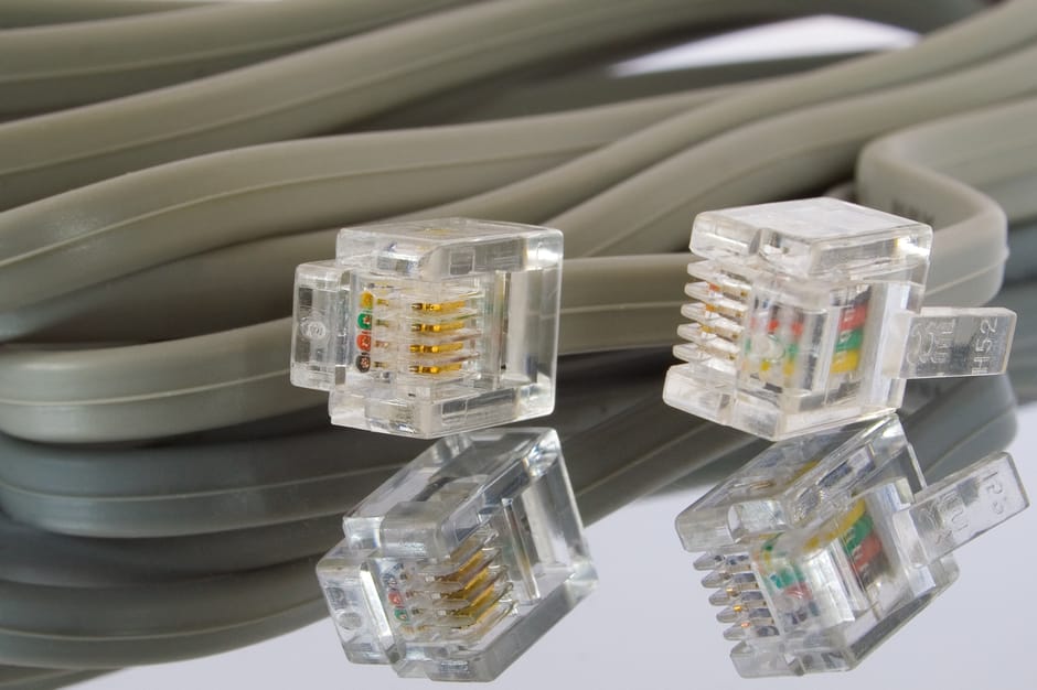 Close-up view of four clear plastic Ethernet keystone jacks with gold-plated contacts, resting on top of a neatly coiled grey Ethernet cable. The keystone jacks are positioned with some lying flat and